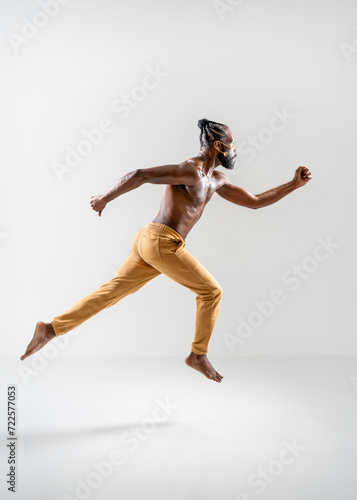 Fototapeta Naklejka Na Ścianę i Meble -  Full length of shirtless African American gay man running isolated on white background. Side view of athletic man jogging in white studio. Equality concept.