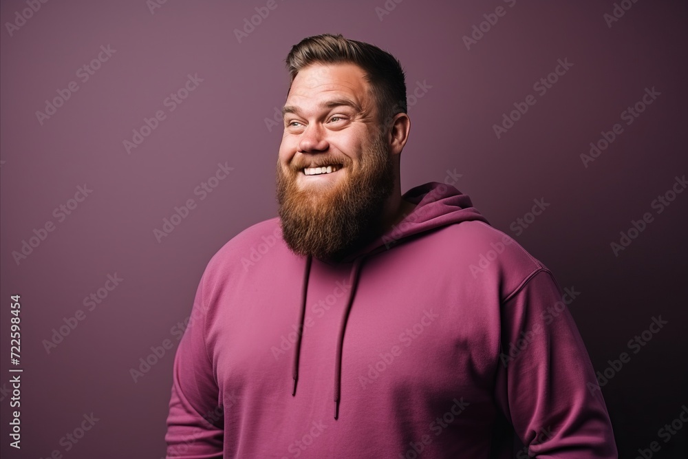 Handsome bearded man in a pink hoodie on a purple background.