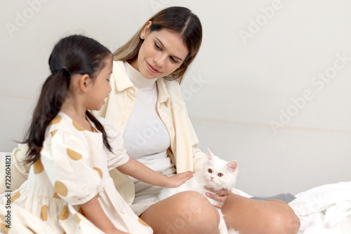 Cute white Persian cat comfortably sitting comfortably sitting in on owner lap hands, mother let her daughter touch gently family pet. Happy fluffy playing with little child girl.