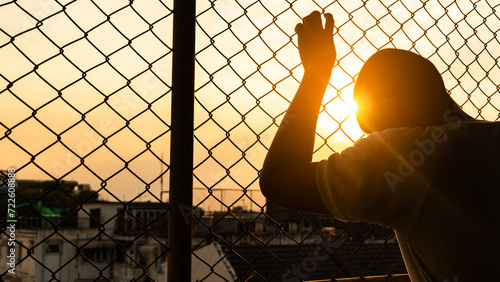 Silhouette of a man behind the fence, Silhouette photo of  feeling upset, sad, unhappy or disappoint crying. Young people mental health care problem lifestyle concept, frustrated standing hopelessly photo