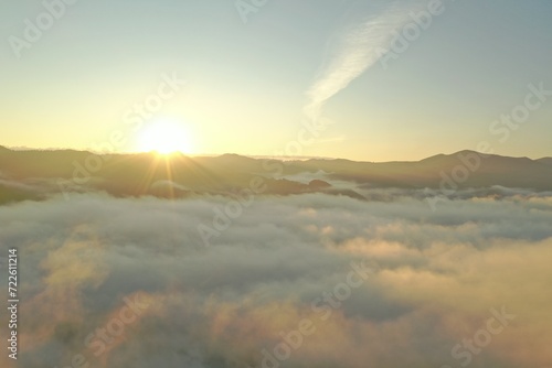 Aerial view of beautiful mountains covered with fluffy clouds at sunrise