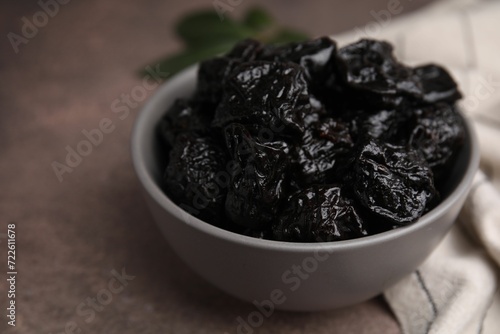 Sweet dried prunes in bowl on brown table, closeup. Space for text