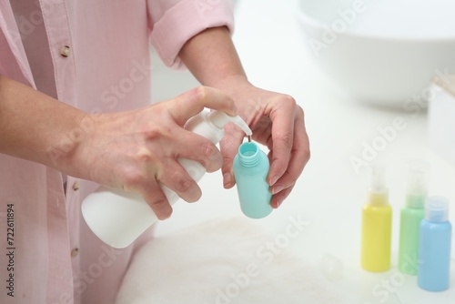 Woman pouring cosmetic product into plastic bottle over white countertop indoors  closeup and space for text. Bath accessories