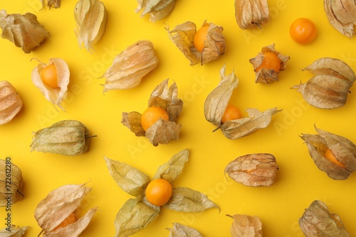 Ripe physalis fruits with calyxes on yellow background, flat lay