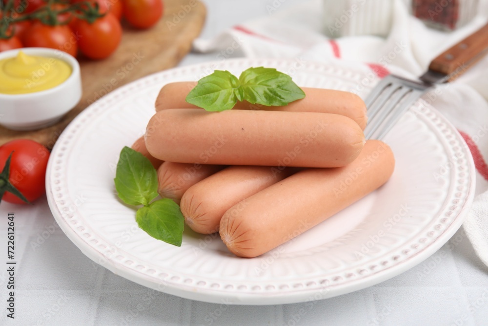 Delicious boiled sausages and basil on white tiled table, closeup