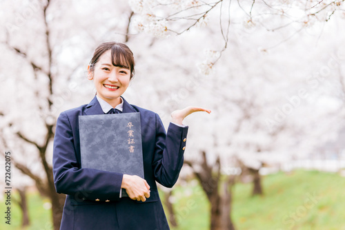 満開の桜の下で卒業証書を持つ高校生・女子高生（卒業生・卒業式・卒業・こちら・おすすめ・案内） 