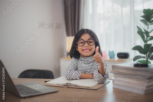 Happy little girl pupil studies online using a laptop at home, smiling small child recommend class or lesson.