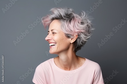 Portrait of a happy middle-aged woman with pink hair on grey background