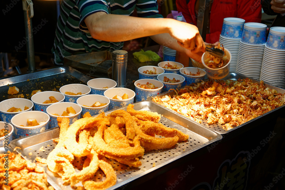Fototapeta premium A stall vendor selling crispy fried seafood in paper cups, one of local people's favorite street-foods, in Flower Night Market, where many traditional snacks can be savored, in Tainan, Taiwan, Asia