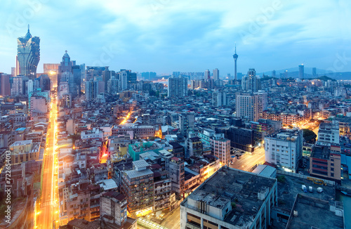 Urban skyline of vibrant Macao City at dusk, with the famous landmarks Grand Lisboa Hotel, a luxury casino resort, and Macau Tower standing among crowded buildings in blue twilight, in Macao, China