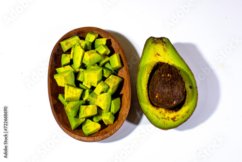 small pieces of green avocado served on a mini wooden plate, and half an avocado next to it