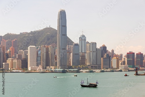 Scenery of Hong Kong on a sunny summer day with boats & ships navigating in Victoria Harbour and the prominent landmark IFC Tower standing among crowded buildings between Victoria Peak and the seaport