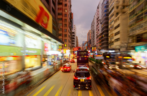 Night scape of trolley cars and double-decker buses dashing on a busy street flanked by office towers and colorful neon signs, in vibrant Mong Kok commercial district, in Kowloon Downtown, Hong Kong photo