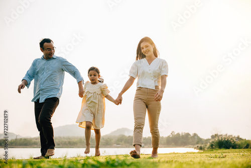 Father and mother with daughter walking together and smiling in a beautiful park on a sunny day, feeling the togetherness and the beauty of the outdoors, Happy family day © sorapop