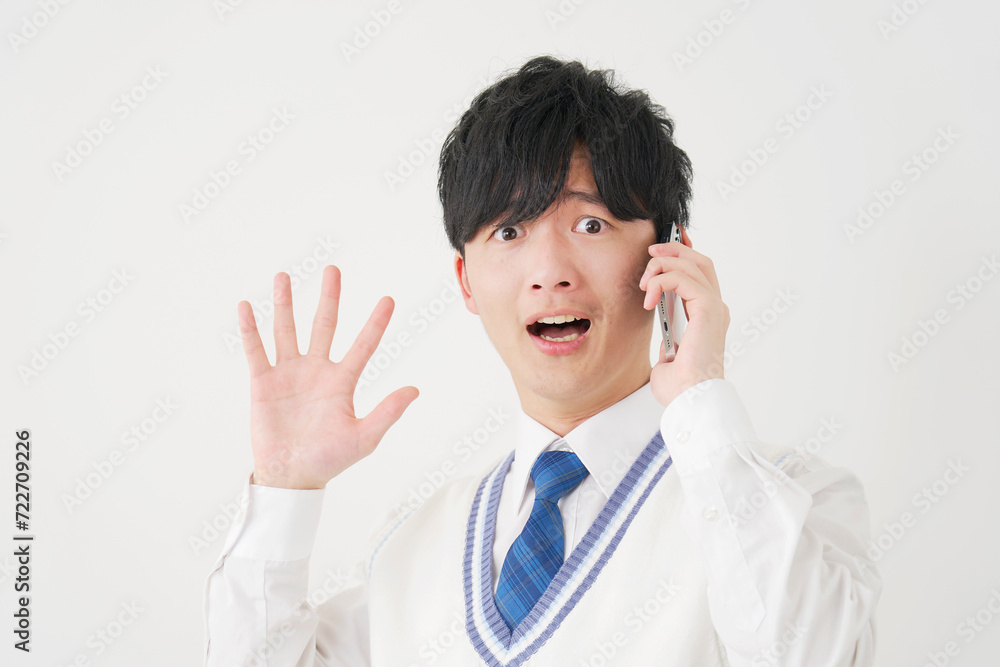 スマートフォンで電話しながら驚く男子高校生　白背景　カメラ目線