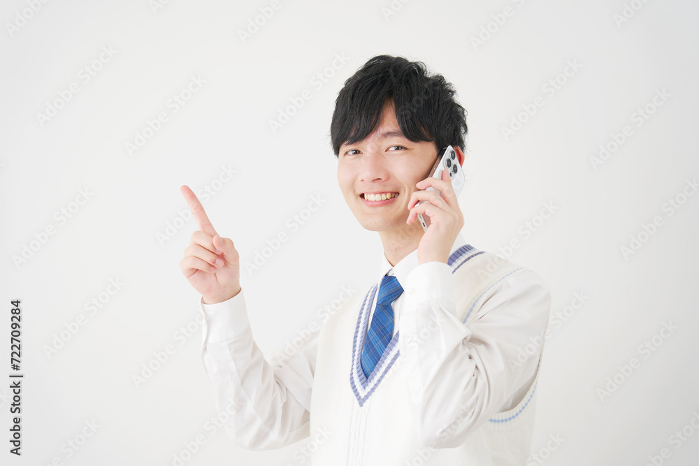 スマートフォンで電話しながら左側を指差す男子高校生 白背景 スマートフォンで電話しながら左側を指差す男子高校生 白背景