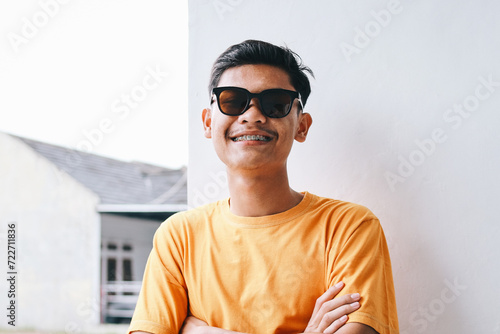 Stylish young guy hipster wear braces teeth and sunglasses standing in crossed arm with happy expression photo