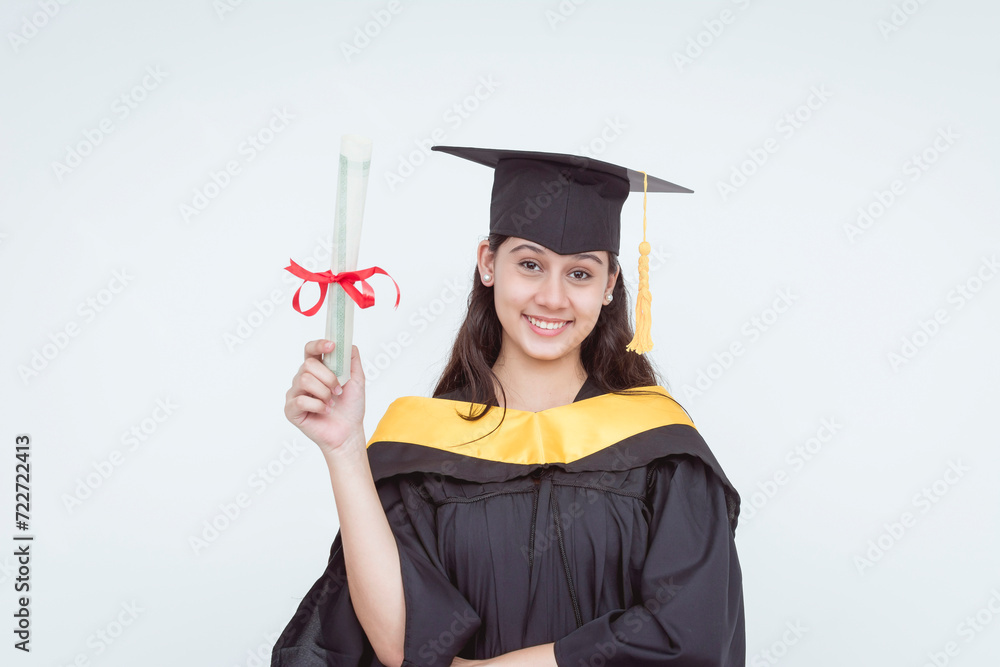 Smiling female bachelor's graduate in cap and gown holding diploma, isolated on white background, expressing accomplishment.