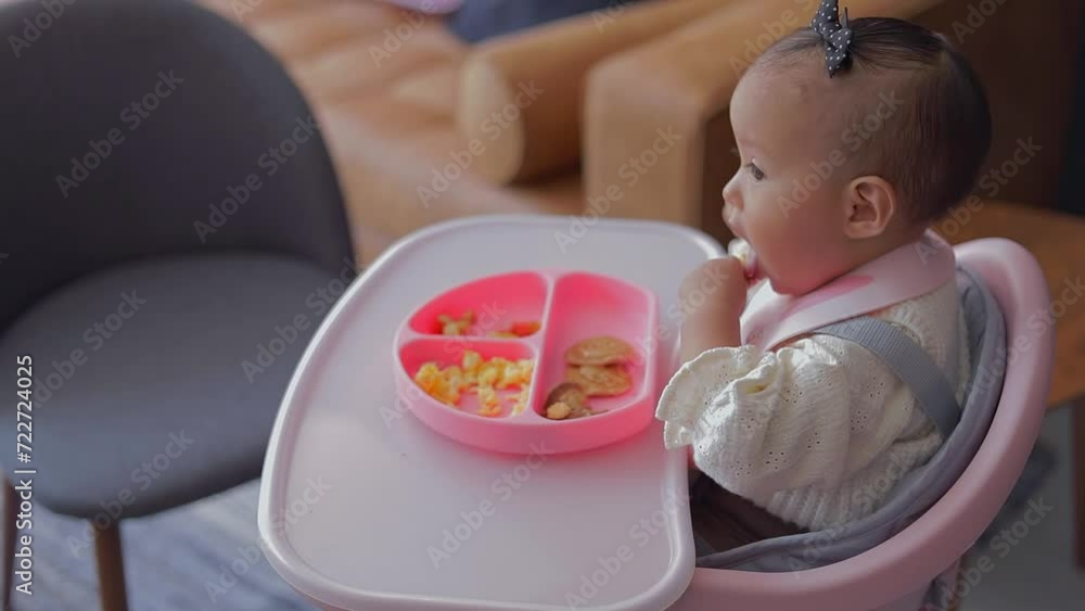 A little girl takes food from her plate with her hands while having breakfast sitting in her chair in the morning. A little girl takes food from her plate with her hands while having breakfast sitting in her chair in the morning.