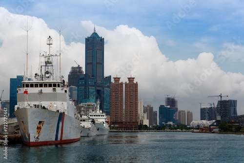 Patrol ships of Coast Guard Administration anchored in Kaohsiung Harbor and the famous landmark 85 Sky Tower standing among skyscrapers in background on a sunny cloudy summer day, in Taiwan, Asia