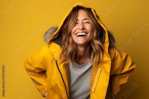Woman with yellow jacket laughing and looking to the side on yellow background © Inigo