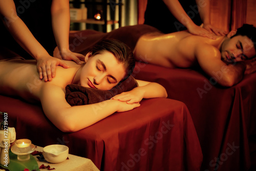 Caucasian couple customer enjoying relaxing anti-stress spa massage and pampering with beauty skin recreation leisure in warm candle lighting ambient salon spa at luxury resort or hotel. Quiescent