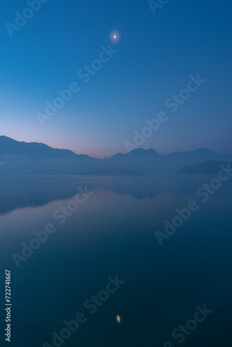 A dawn at Sun Moon Lake in Nantou County, Taiwan. A beautiful view with half moon over a lake in the mountains. Blue sky with reflection on the lake