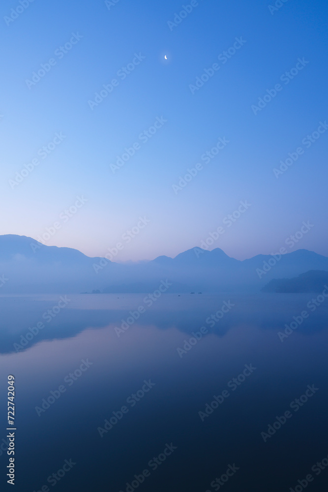 A dawn at Sun Moon Lake in Nantou County, Taiwan. A beautiful morning with half moon over a lake in the mountains. Blue sky with reflection on the lake