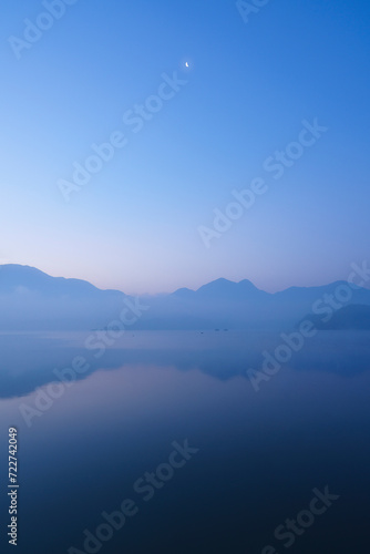 A dawn at Sun Moon Lake in Nantou County, Taiwan. A beautiful morning with half moon over a lake in the mountains. Blue sky with reflection on the lake photo