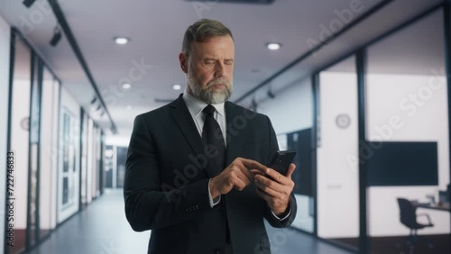 Wallpaper Mural Portrait of a Respectable Adult Man in a Tailored Business Suit Using Smartphone, Smiling while Walking in a Corporate Office Hallway. Successful Businessman Communicating Over Text Messages Torontodigital.ca