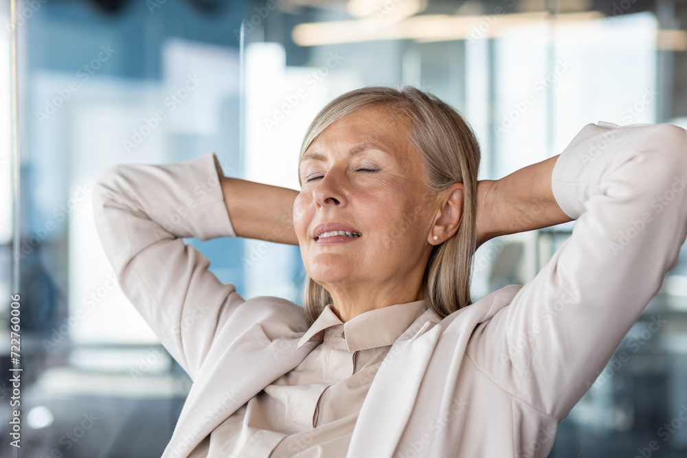 Close up of mature businesswoman sitting in modern office with hands behind head and relaxing after stressful day. Senior female in office wear resting with closed eyes and making break from work. Close up of mature businesswoman sitting in modern office with hands behind head and relaxing after stressful day. Senior female in office wear resting with closed eyes and making break from work.