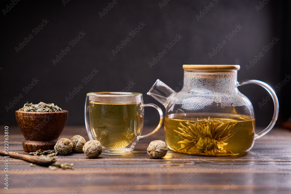 Teapot and glass cup with blooming tea flower inside on a wooden table