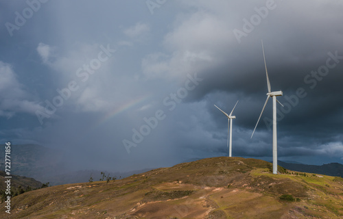Wind turbines on landscape with storm clouds and rainbow.