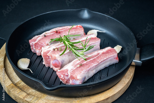 Closeup view of raw ribs with rosemary and spices in a round grill pan