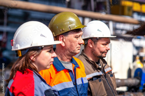 Professional team and portrait of an engineer standing in a group of out-of-focus workers at an industrial manufacturing factory. They workat at metallurgical or oil refinery plant.Inspection check.