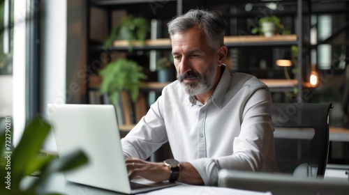 A man in his middle years is engaged with his laptop in his contemporary workspace.