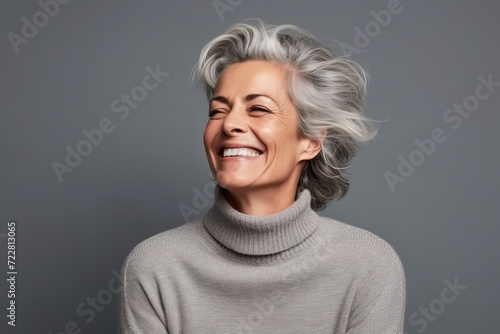 Portrait of a happy senior woman with grey hair laughing against grey background