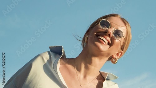 Beautiful young happy woman, smiling in sunglasses, against sky background. Fashion female model in stylish clothes in summer outdoors