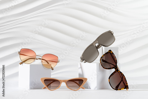 Photos Set of different trendy sunglasses on podiums on white background