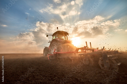 Tractor plowing field at sunset photo