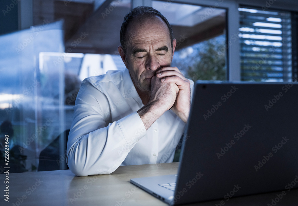 Mature freelancer napping near laptop at home office Mature freelancer napping near laptop at home office