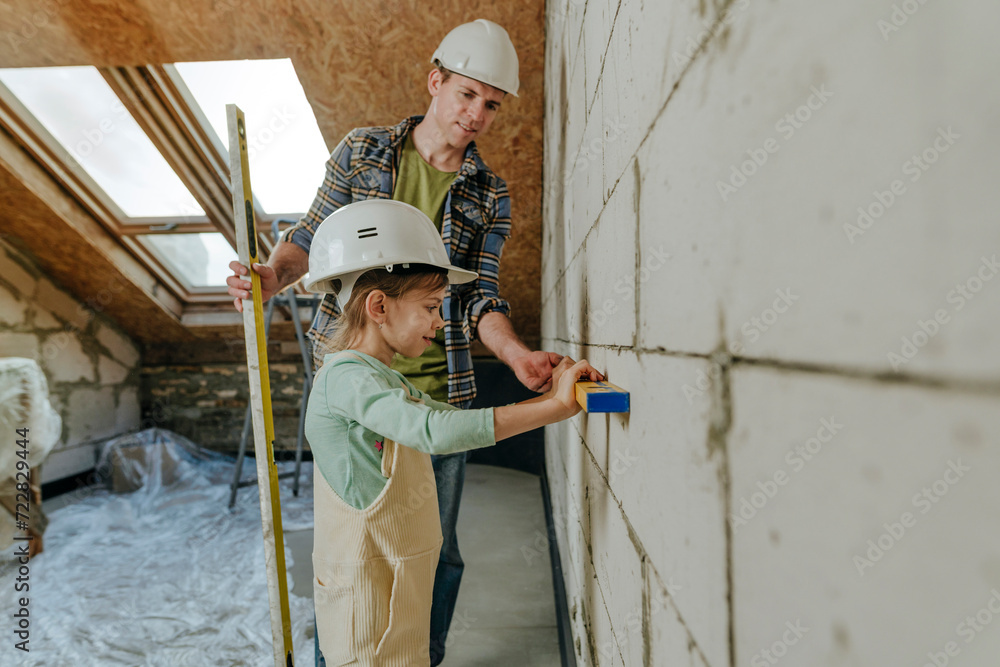 Father and daughter using leveling tool on wall in room under renovation Father and daughter using leveling tool on wall in room under renovation