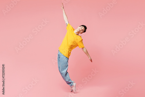 Full body young man wears yellow t-shirt casual clothes stand on toes with outstretched hands lean back look camera isolated on plain pastel light pink background studio portrait. Lifestyle concept photo