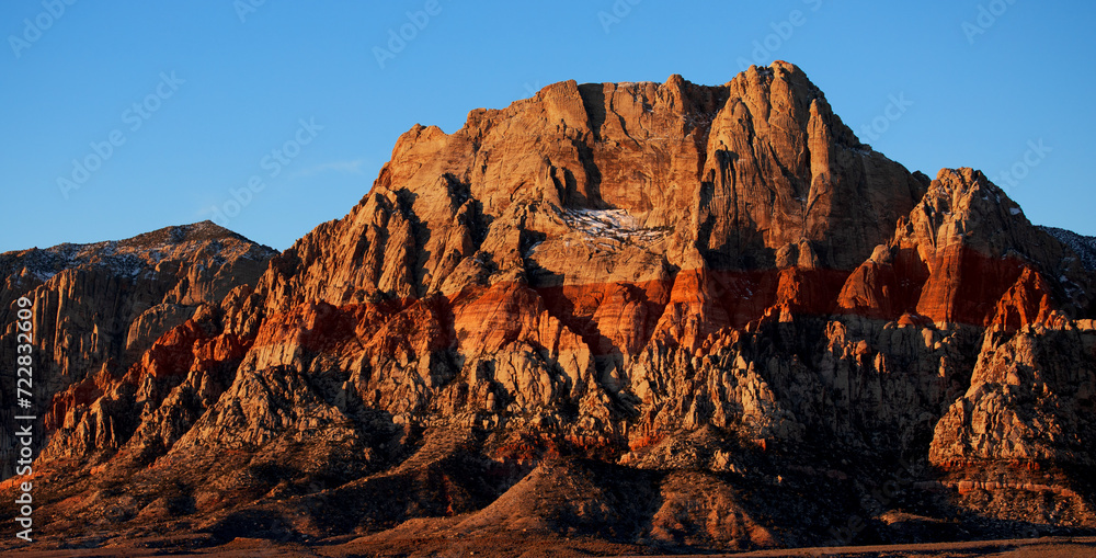 Lever de soleil sur Red Rock Mountain, Las Vegas, Nevada, États-Unis d'Amérique. Montagne à la roche rouge et jaune s'élevant au milieu d'une plaine désertique avec traces de neige sur la paroi. - obrazy, fototapety, plakaty 
