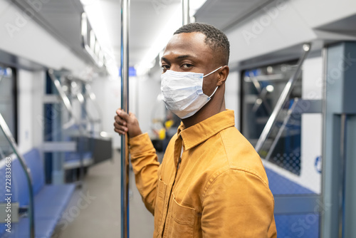 Portrait of an African-American man in a protective mask who is riding in a subway car. A man looks at the camera