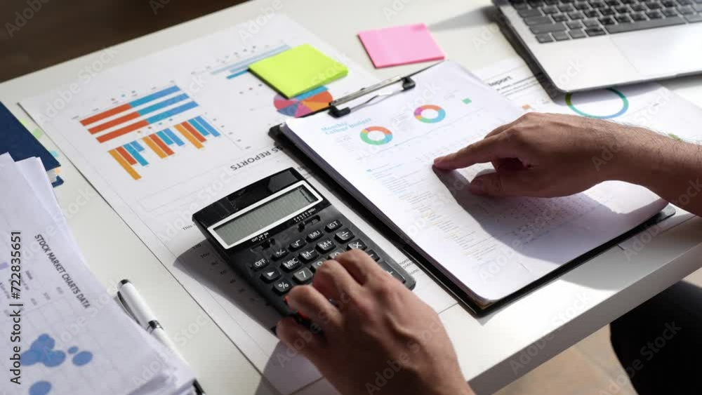 Asian male finance staff is calculating by using a calculator. Investment results to report to his boss at the meeting. On the table in the office, is the concept of calculating investment results. Asian male finance staff is calculating by using a calculator. Investment results to report to his boss at the meeting. On the table in the office, is the concept of calculating investment results.
