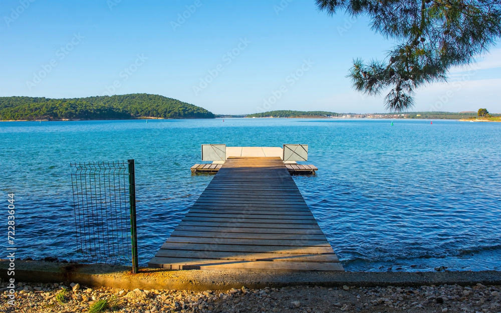 Obraz premium A swimming pier on the coast of Kasteja Forest Park - Park Suma Kasteja - in Medulin, Istria, Croatia. Premantura peninsula is in the background. December