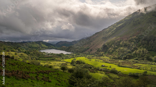 Moody clouds roll over a lush, green valley, surounded by the mountains of Snowdonia, north Wales, UK, with the sun highlighting parts of the vally floor