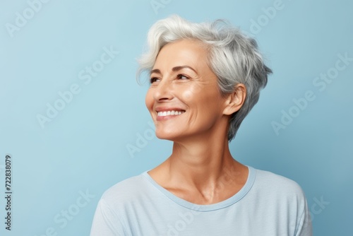 smiling senior woman with grey hair looking up at copy space over blue background