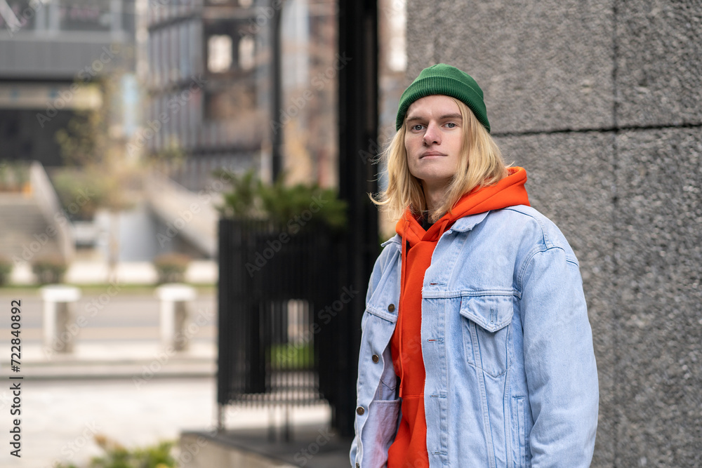 City portrait of handsome long-haired hipster guy wearing trendy stylish outfit, standing in city street, looking at camera. Slim fashionable male zoomer in colorful clothes represents generation z City portrait of handsome long-haired hipster guy wearing trendy stylish outfit, standing in city street, looking at camera. Slim fashionable male zoomer in colorful clothes represents generation z